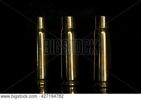 Spent Cartridges On A Black Background. Three Empty Cartridge Cases Are Lined Up Side By Side. Close