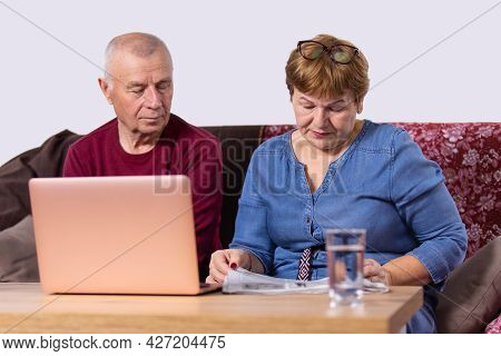 Aged Couple Going About Their Business, Woman Reading A Newspaper And Man Opened Laptop And Sitting 
