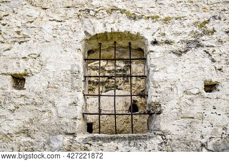 Arched Window With Metal Bars In Old Stonework. The Texture Of The Old Dilapidated Masonry. The Anci
