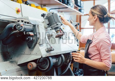 Woman cobbler working on machine in her shoemaker workshop