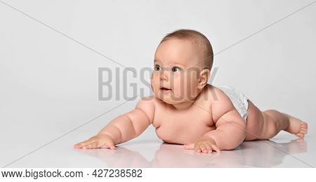 Six Month Old Baby Girl In A Diaper Lying And Looking With Interest To The Side On A White Backgroun