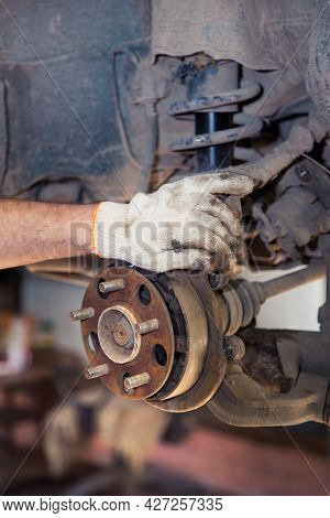 A Mans Gloved Hand Holds A Rusty Car Wheel Hub. In The Garage, A Man Changes Parts On A Vehicle. Sma
