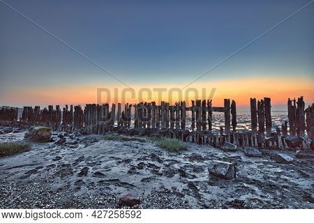 View Of The Wadden Sea During Sunset, At Low Tide. Wooden Posts As A Silhouette In The Mud. Unesco. 
