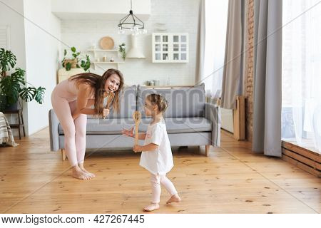 Mommy Sings A Song Using A Kitchen Spatula Like Microphone With Little Cute Daughter In Cozy Light L
