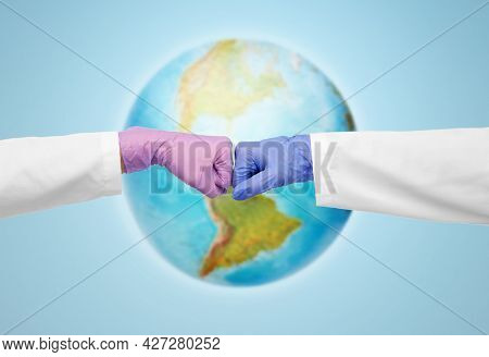 medicine, health protection and healthcare concept - hands of doctors in gloves make fist bump gesture over earth globe on blue background