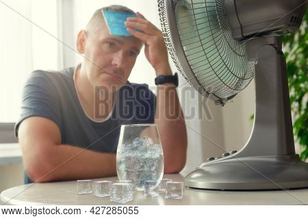 Man suffers from heat while sitting in the oom and tries to cool off by the fan