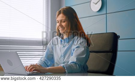 Smiling woman general practitioner communicates with patients online typing on grey laptop and smiling at table in doctor office