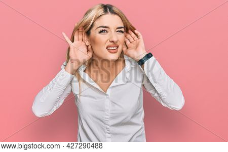 Young caucasian woman wearing casual clothes trying to hear both hands on ear gesture, curious for gossip. hearing problem, deaf 