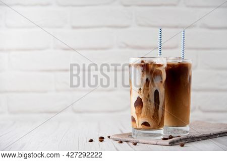 Iced Coffee Latte Cappuccino In A Tall Glass With Cream Or Milk And coffee beans And Straws On A Whi