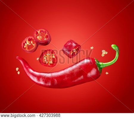 Fresh red chilli pepper and cross sections of chilli pepper with seeds floating in the air. Red background.