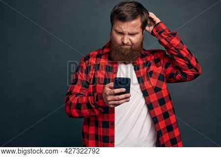 Young Modern Man In Red Checkered Shirt Using Smartphone With Busy Serious Expression, Holding Mobil