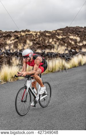 Triathlon cycling race time trial triathlete man cyclist riding road bike in Hawaii race in volcanic landscape. Fitness active lifestyle vertical crop.