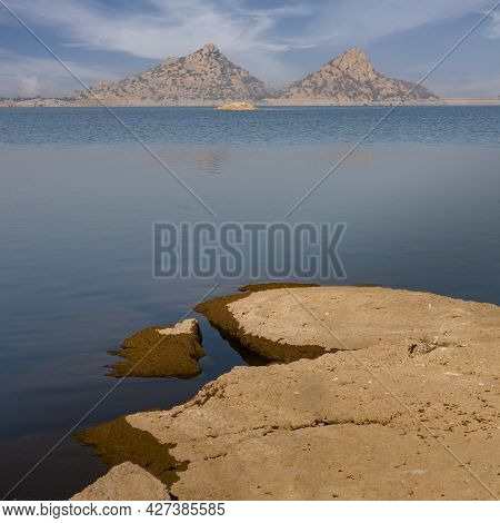 Landscape Of Jawai Dam With Water, Clear Blue Sky And Aravalli Mountain Ranges With Its Reflection I