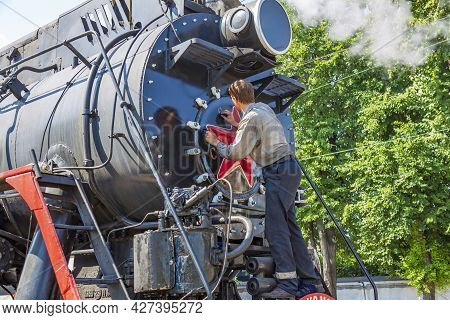 Worker Washes A Black Retro Steam Locomotive At The Railway Station