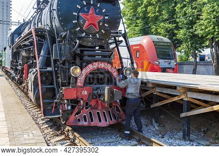 Worker Washes A Black Retro Steam Locomotive At The Railway Station