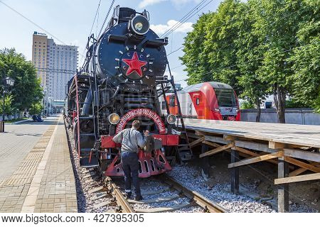Worker Washes A Black Retro Steam Locomotive At The Railway Station