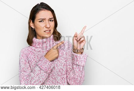 Young caucasian girl wearing wool winter sweater pointing aside worried and nervous with both hands, concerned and surprised expression 