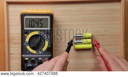 Testing AA battery cells with digital multimeter tool, voltage check showing low value, battery is used and mostly discharged