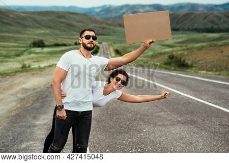 A Man And A Woman Are Hitchhiking. Wanderlust, Autostop Journey Concept. Young People Traveling Hitc