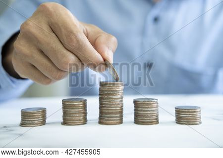 Businessman Saving Money Concept. Hand Holding Coins Putting In Jug Glass