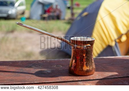 Copper Turkish Coffee Cezve Against Blurred Campsite Background. Making Coffee In Cezve On In Outdoo