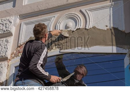 Man Restores Facade Of An Old Building With Stucco: Applies Plaster With Spatula And Trowel. Vyshny 