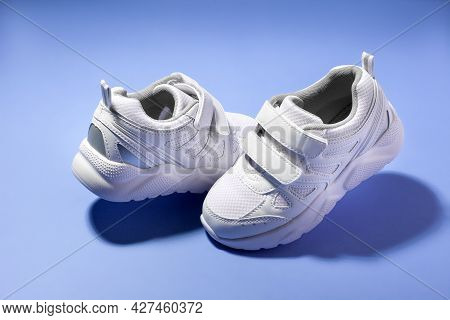 White Kid Floating Sneakers With Velcro Fasteners Face Each Other Isolated On Apurple Background Wit