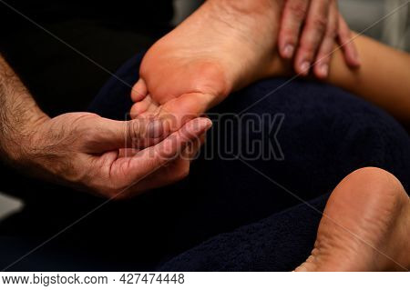 Close Up Of Therapist's Hands Massaging Female Foot.reflexologist Applying Pressure To Foot With Thu