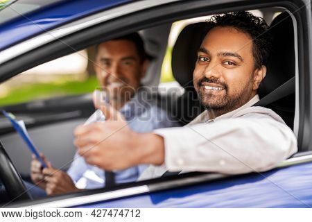 driver courses, exam and people concept - happy smiling indian man showing thumbs up and driving school instructor with clipboard in car