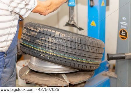 Mechanic Changing Tire In Car Service. Tire Rotation Machine.car Mechanic Mounts Tire On Wheel In A 