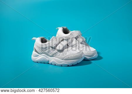 An Ad For White Teen Sneakers Standing Sideways On An Isolated Blue Paper Background With Harsh Sunl