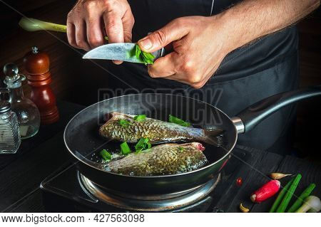 Chef Prepares Fresh Fish In A Pan With Young Green Onion. Preparation For Cooking Fish Food. Working