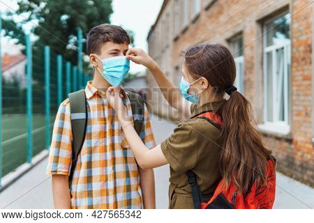 schoolboy and schoolgirl posing on the way to school, wearing a protective mask on their faces from a coronavirus infection, education and back to school concept