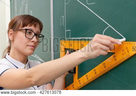 School Teacher Young Woman In The Class At The Blackboard Draws A Triangle With A Ruler. Portrait. C
