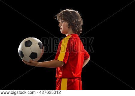 Portrait Of Little Boy, Football Soccer Player Posing With Football Ball Isolated On Dark Studio Bac