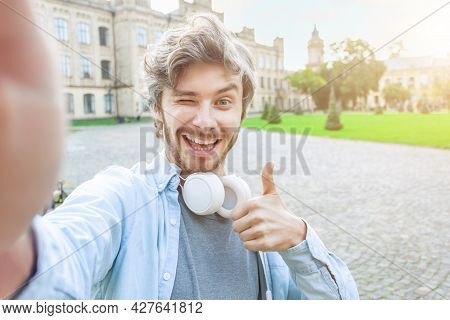 Portrait Of Happy Young Man Is Making Selfie Photo With Thumb Up On Background Of University Campus.