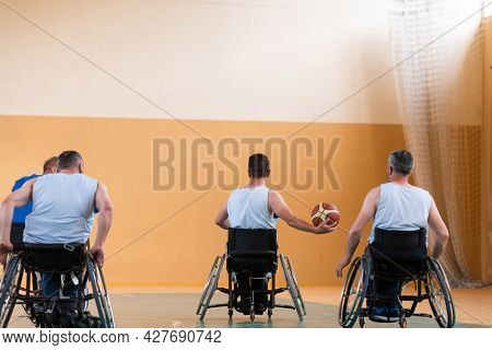 Disabled War veterans mixed race opposing basketball teams in wheelchairs photographed in action while playing an important match in a modern hall. 