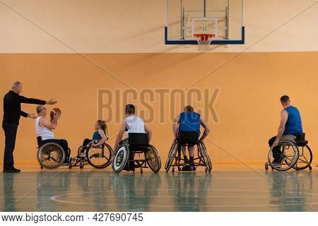 Disabled War veterans mixed race opposing basketball teams in wheelchairs photographed in action while playing an important match in a modern hall. 