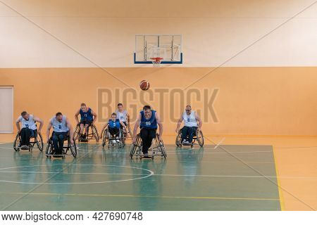 Disabled War veterans mixed race opposing basketball teams in wheelchairs photographed in action while playing an important match in a modern hall. 