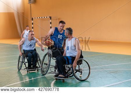 Disabled War veterans mixed race opposing basketball teams in wheelchairs photographed in action while playing an important match in a modern hall. 