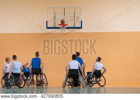 Disabled War veterans mixed race opposing basketball teams in wheelchairs photographed in action while playing an important match in a modern hall. 