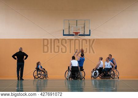 Disabled War veterans mixed race opposing basketball teams in wheelchairs photographed in action while playing an important match in a modern hall. 