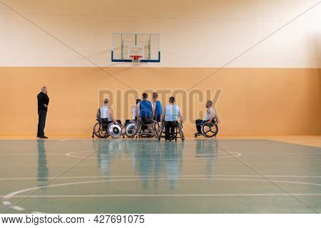 Disabled War veterans mixed race opposing basketball teams in wheelchairs photographed in action while playing an important match in a modern hall. 