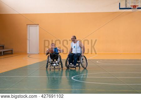 Disabled War veterans mixed race opposing basketball teams in wheelchairs photographed in action while playing an important match in a modern hall. 