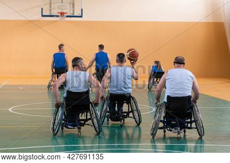 Disabled War veterans mixed race opposing basketball teams in wheelchairs photographed in action while playing an important match in a modern hall. 