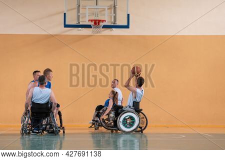 Disabled War veterans mixed race opposing basketball teams in wheelchairs photographed in action while playing an important match in a modern hall. 