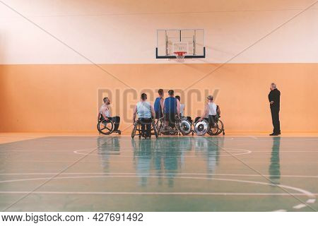 Disabled War veterans mixed race opposing basketball teams in wheelchairs photographed in action while playing an important match in a modern hall. 