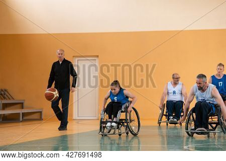 Disabled War veterans mixed race opposing basketball teams in wheelchairs photographed in action while playing an important match in a modern hall. 
