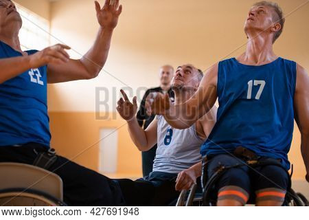 Disabled War veterans mixed race opposing basketball teams in wheelchairs photographed in action while playing an important match in a modern hall. 