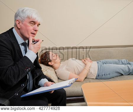 Caucasian Woman Lies On A Couch At A Reception With A Psychotherapist. An Elderly Man Works As A Psy